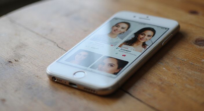 Smartphone zeigt Dating-Profile auf einem hölzernen Tisch.